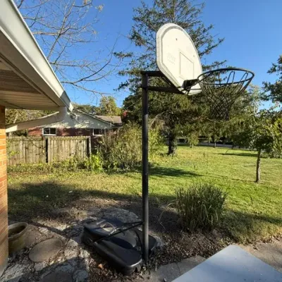 Sale Photo Thumbnail #489: Portable outdoor basketball hoop with a plastic fillable base and metal chain net, showing signs of weathering.