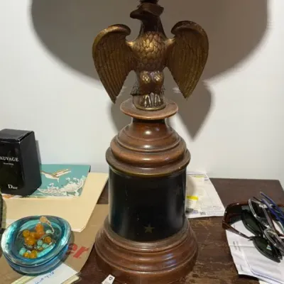Sale Photo Thumbnail #289: Vintage table lamp featuring a brass spread-eagle finial mounted on a turned wooden base with star details, shown alongside small household accessories.