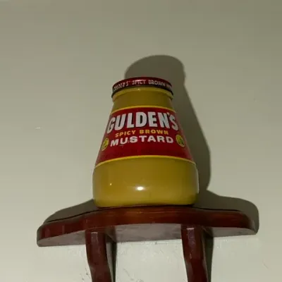 Sale Photo Thumbnail #311: Sealed jar of Gulden's Spicy Brown Mustard resting on a small wall-mounted wooden display shelf.