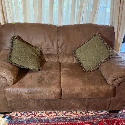 Sale Photo Thumbnail #254: Brown microfiber recliner loveseat featuring padded roll arms and two green accent pillows with fringe trim.