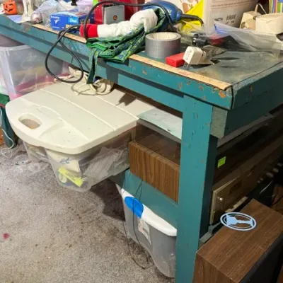 Sale Photo Thumbnail #373: Rustic teal-painted wooden workbench cluttered with office supplies, tapes, and electronics, featuring plastic storage totes and vintage audio equipment underneath.
