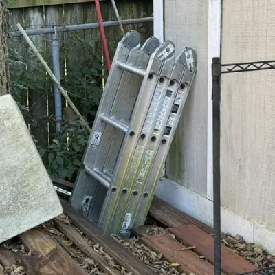 Sale Photo Thumbnail #502: Folded aluminum multi-position articulating ladder resting outdoors against a shed.
