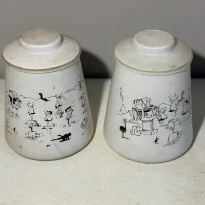 Sale Photo Thumbnail #416: Pair of vintage glass canisters featuring black cartoon illustrations, showing moderate surface wear and scuffing.