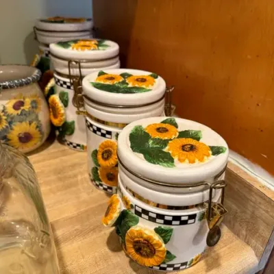 Sale Photo Thumbnail #320: Set of ceramic kitchen canisters featuring raised sunflower motifs and black-and-white checkered trim with metal wire bail-locking lids.
