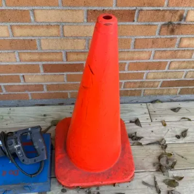 Sale Photo Thumbnail #203: Tall bright orange safety cone alongside a handheld reciprocating saw sitting on a blue metal toolbox against a brick wall.