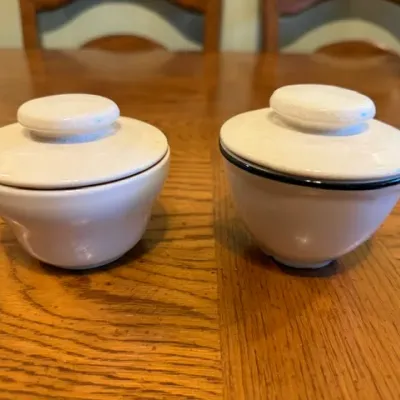 Sale Photo Thumbnail #28: Pair of small cream-colored ceramic covered bowls with fitted lids, set on a wooden surface.