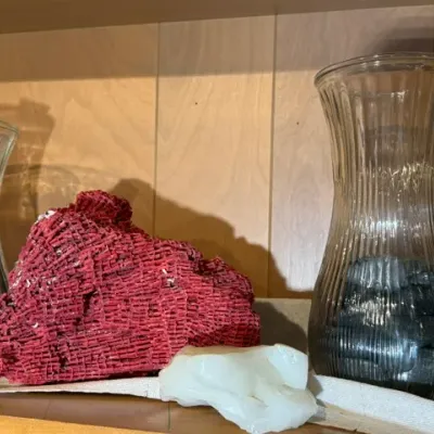 Sale Photo Thumbnail #118: Natural red pipe coral specimen displayed alongside a white quartz cluster and two ribbed clear glass vases filled with black river stones.
