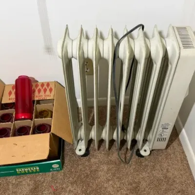 Sale Photo Thumbnail #354: Portable oil-filled electric radiator heater alongside a cardboard box filled with vintage red glass prayer candle jars.