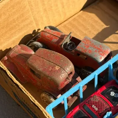 Sale Photo Thumbnail #448: Vintage die-cast metal toy cars with heavily worn red paint, displayed alongside other toy vehicles in a cardboard box.