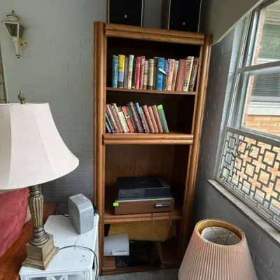Sale Photo Thumbnail #182: Tall oak bookcase filled with books, audio equipment, and electronics, shown alongside a traditional table lamp and shade.