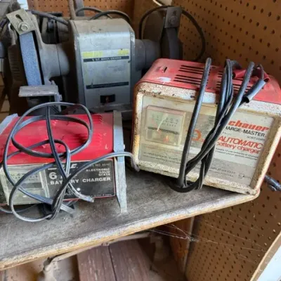 Sale Photo Thumbnail #211: Vintage bench grinder alongside two retro Schauer automatic battery chargers with power cables, showing wear from age and workshop use.