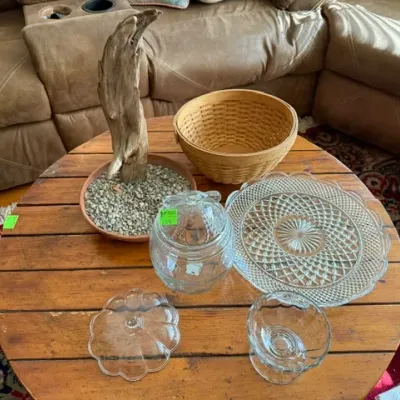 Sale Photo Thumbnail #132: Rustic wooden coffee table displaying a collection of home decor and glassware, including a driftwood accent in a gravel tray, a woven basket, a cut-glass tray, and glass serving pieces.