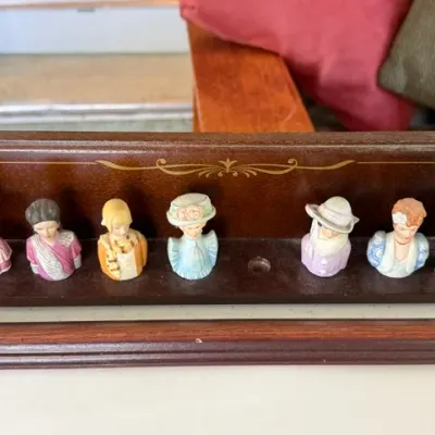 Sale Photo Thumbnail #248: Collection of vintage porcelain lady bust thimbles displayed on a wooden stand with gold stenciled details.