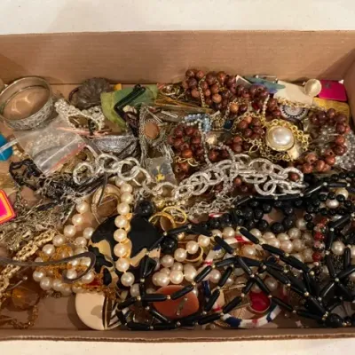 Sale Photo Thumbnail #67: Cardboard box filled with assorted vintage costume jewelry, including beaded necklaces, faux pearls, chains, bangles, and brooches.
