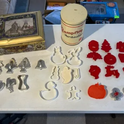 Sale Photo Thumbnail #240: Collection of vintage kitchen collectibles, featuring a Campfire Marshmallows tin, a decorative tin box, and various metal and plastic cookie cutters.