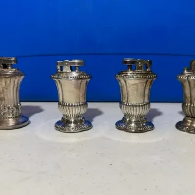 Sale Photo Thumbnail #54: Set of four vintage silver-plated urn-style table lighters with decorative gadrooned bases and tarnished finish.