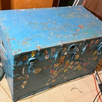 Sale Photo Thumbnail #395: Vintage painted blue steamer trunk featuring metal hardware latches and colorful novelty stickers across the front panel.