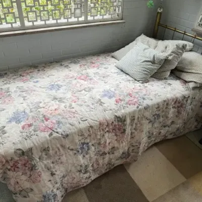 Sale Photo Thumbnail #179: Twin bed featuring a brass headboard, dressed in a pastel floral comforter and striped throw pillows.
