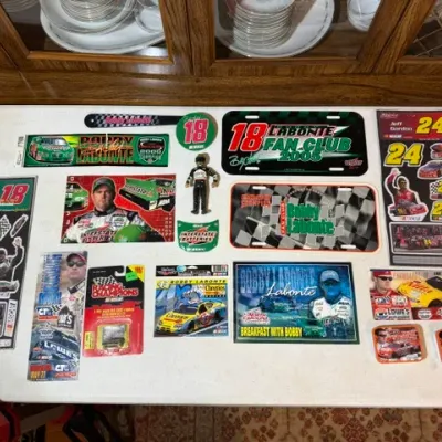 Sale Photo Thumbnail #83: Collection of NASCAR memorabilia focusing primarily on Bobby Labonte and Jeff Gordon, including vanity license plates, sticker sheets, die-cast vehicles, and an action figure.