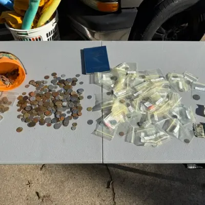 Sale Photo Thumbnail #440: Large collection of loose and bagged foreign and domestic coins spread out on a gray folding table alongside currency and a coin album.