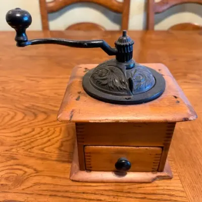 Sale Photo Thumbnail #29: Vintage manual coffee grinder featuring a dovetail-jointed wooden box, a small collection drawer, and a cast iron crank mechanism with embossed floral details on the dome cover.