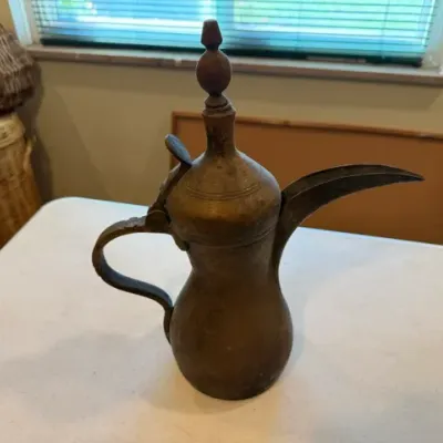 Sale Photo Thumbnail #40: Antique Middle Eastern brass dallah coffee pot featuring a long, curved spout, hinged lid with decorative finial, and an aged patina.