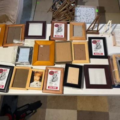 Sale Photo Thumbnail #213: Large assortment of wooden and composite picture frames in various finishes, shapes, and sizes arranged on a folding table alongside miniature display easels.