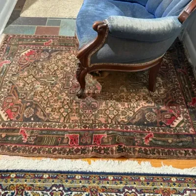 Sale Photo Thumbnail #136: Hand-knotted Persian or Oriental area rug with geometric motifs and fringe, paired with a blue velvet channel-tufted armchair featuring carved wooden legs.
