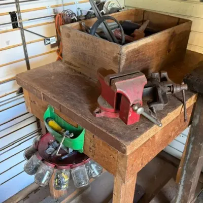 Sale Photo Thumbnail #210: Rustic wooden workbench equipped with a red bench vise, a vintage wooden crate, and a revolving glass jar hardware organizer underneath.