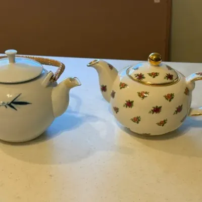 Sale Photo Thumbnail #24: Pair of vintage ceramic teapots, including an Asian-style teapot with a wicker handle and blue bamboo motif alongside a floral-patterned teapot with gold trim.