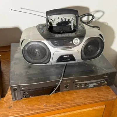 Sale Photo Thumbnail #330: Dusty silver Sanyo portable CD player and cassette boombox resting atop a black Go-Video dual deck VCR.