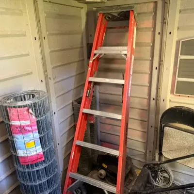 Sale Photo Thumbnail #283: Red Keller fiberglass stepladder alongside a roll of welded wire mesh fencing stored inside a shed.
