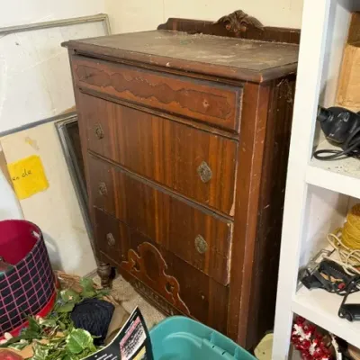 Sale Photo Thumbnail #376: Vintage dark wood four-drawer chest with decorative carved trim and metal hardware, showing heavy surface wear and dust.