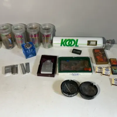 Sale Photo Thumbnail #424: Collection of vintage tobacciana items, including Joe Camel Club plastic tumblers, various pocket lighters, cigarette matchbooks, and branded Kool and Camel ashtrays.