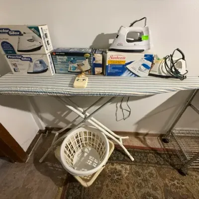 Sale Photo Thumbnail #389: Collection of laundry supplies including a striped ironing board, plastic laundry baskets, and several vintage clothing irons with original boxes.