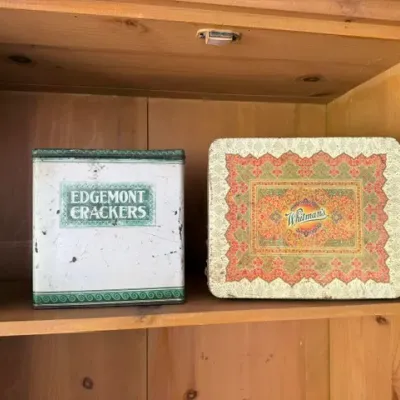 Sale Photo Thumbnail #486: Vintage tin collection on a wooden shelf, including an Edgemont Crackers tin and an ornate Whitman's candy tin.