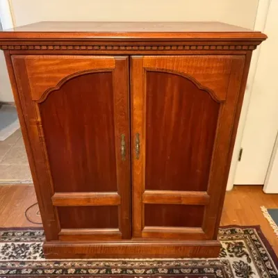 Sale Photo Thumbnail #161: Traditional cherry-finished wooden media cabinet or armoire featuring arched double doors and brass hardware.