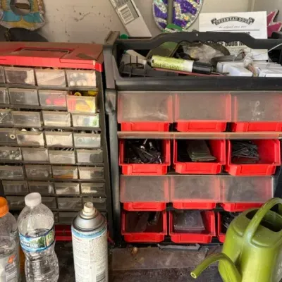 Sale Photo Thumbnail #481: Two plastic multi-drawer parts cabinets filled with hardware, paired with assorted garage items including a green watering can.