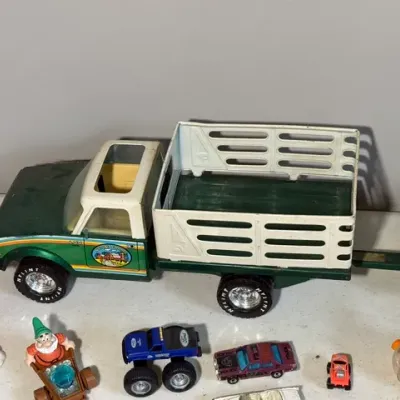 Sale Photo Thumbnail #421: Vintage Nylint pressed-steel stake bed farm truck with trailer, accompanied by various die-cast vehicles and plastic toy figurines showing minor play wear.