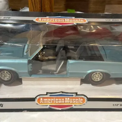 Sale Photo Thumbnail #107: American Muscle 1/12 scale die-cast metal 1964 Pontiac GTO convertible model in light blue, new in original packaging.
