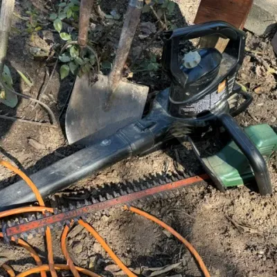 Sale Photo Thumbnail #201: Selection of outdoor power equipment and garden tools, including an electric leaf blower, hedge trimmer, shovel, and orange extension cord.