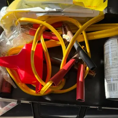 Sale Photo Thumbnail #473: Black portable carrying case filled with automotive emergency supplies, including yellow jumper cables, a red plastic funnel, and an aerosol can.