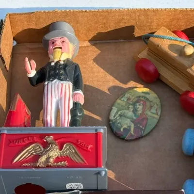 Sale Photo Thumbnail #445: Cast iron Uncle Sam mechanical bank, accompanied by a small oval religious icon pin and vintage wooden toy trains in a box.