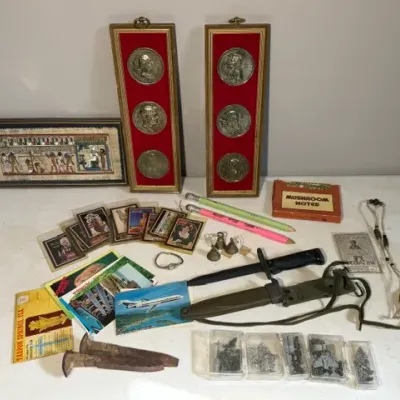 Sale Photo Thumbnail #425: Collection of eclectic collectibles, including framed wall plaques with large commemorative medallions, framed Egyptian papyrus art, vintage bayonet with sheath, postcards, and small boxed items.