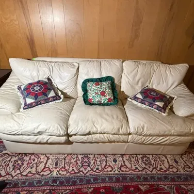 Sale Photo Thumbnail #251: Off-white leather vintage three-cushion sofa styled with patterned throw pillows, set against wood-paneled walls.