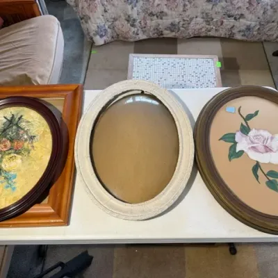Sale Photo Thumbnail #191: Collection of framed vintage art pieces and empty picture frames, including a floral impasto painting and an oval rose artwork, arranged on a folding table.