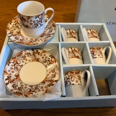 Sale Photo Thumbnail #35: Twelve-piece fine porcelain espresso set featuring a brown and gold scrollwork pattern, displayed in its original packaging.