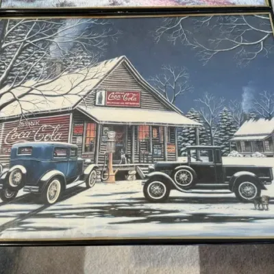 Sale Photo Thumbnail #238: Framed nostalgic Coca-Cola artwork featuring a snowy winter scene at a general store with vintage automobiles, presented in a black glass-front frame.