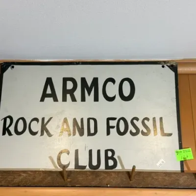 Sale Photo Thumbnail #129: Vintage painted metal sign for the "ARMCO Rock and Fossil Club," featuring black lettering on a light background with visible edge wear.