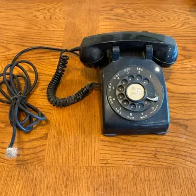 Sale Photo Thumbnail #20: Vintage black Western Electric Model 500 rotary dial landline telephone resting on a wooden table.